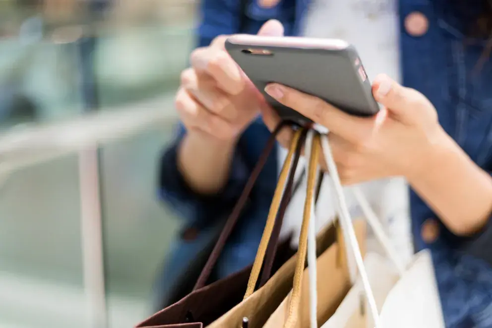 close up of person using cell phone holding shopping bags close up of person using cell phone holding shopping bags