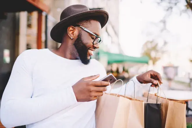 smiling man looking through shopping bags and using cell phone smiling man looking through shopping bags and using cell phone